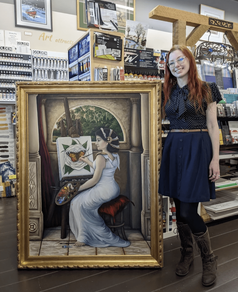 photo of Vanessa Tomada, standing beside her large painting of a woman in a white dress, painting at an easel